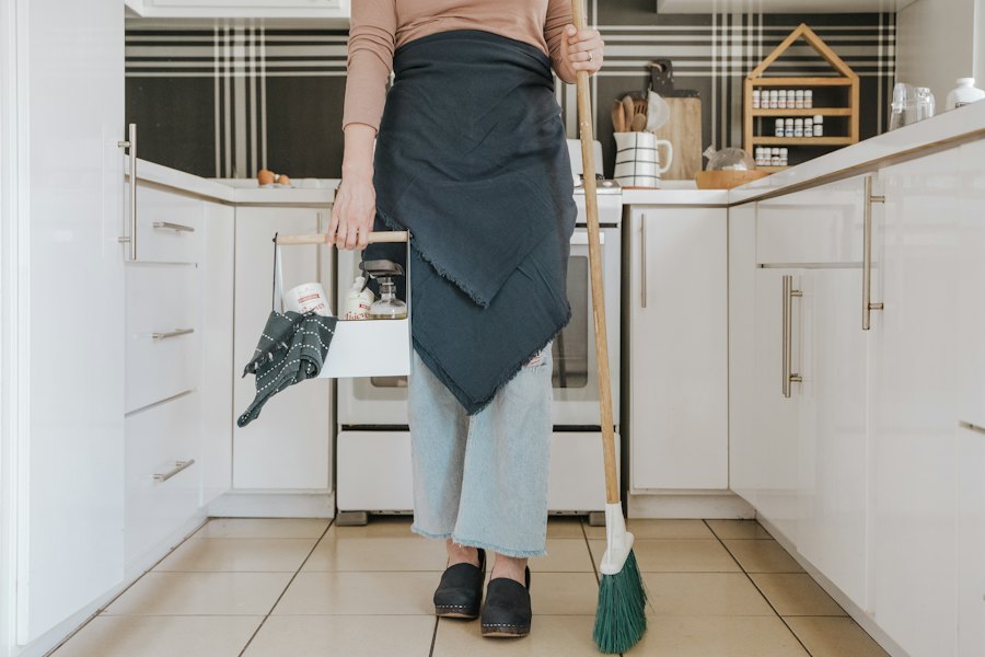A cleaner standing in a bright kitchen holding a broom