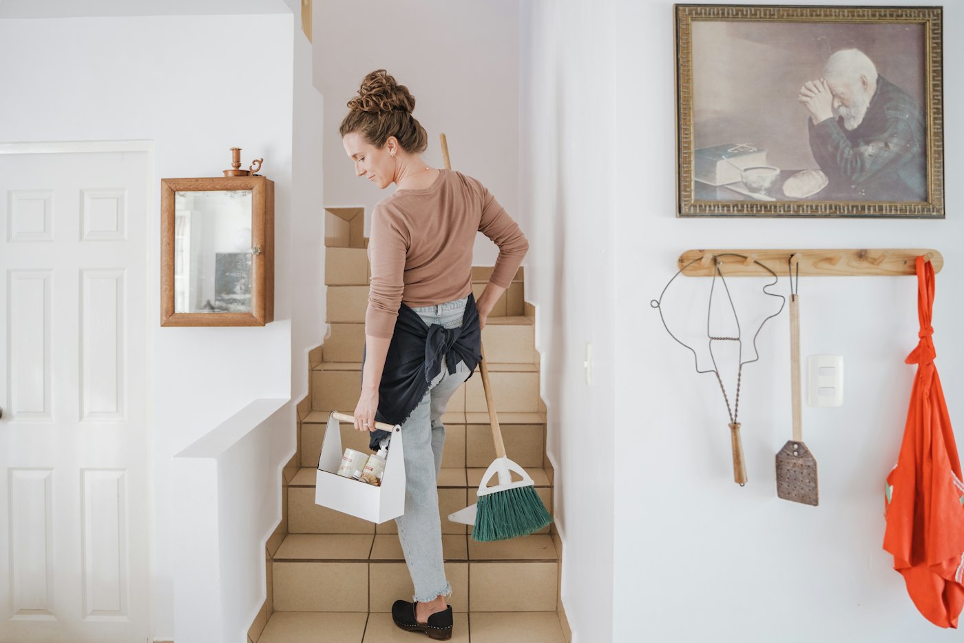 A cleaner carrying a caddy of supplies up the stairs of a bright home